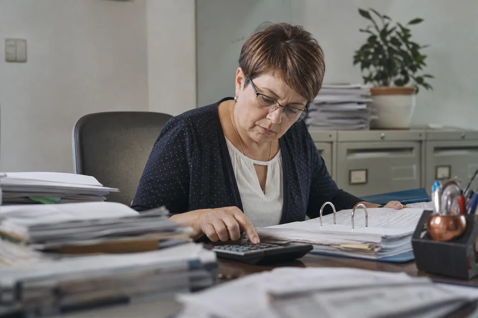 Księgowa z kalkulatorem i segregatorem faktur w małym biurze rachunkowym